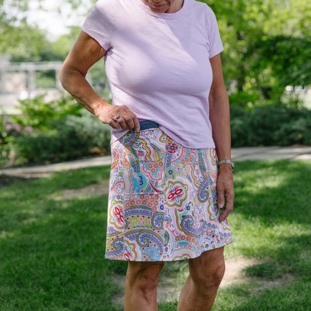 woman with soft pink top and colorful paisley pattern skirt pulling phone from pocket
