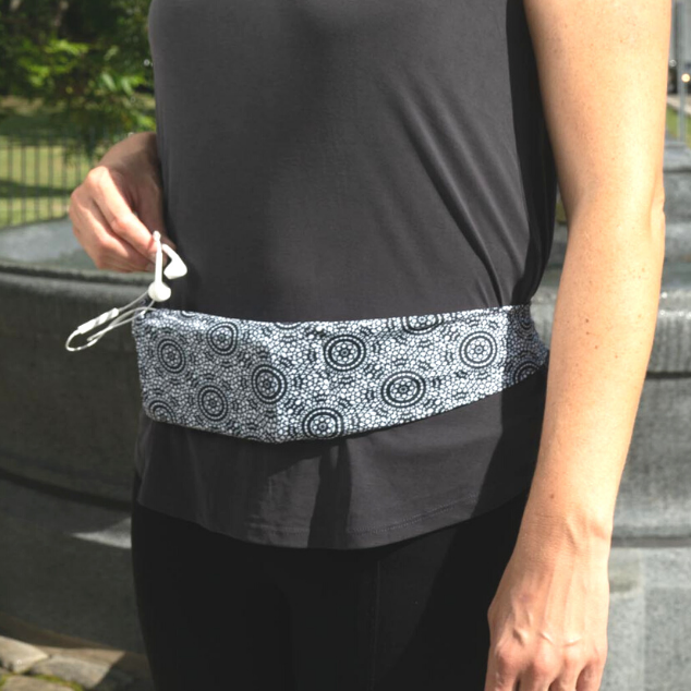 Close up of woman wearing black top and leggings with BOHO belt around waist and holding ear buds.