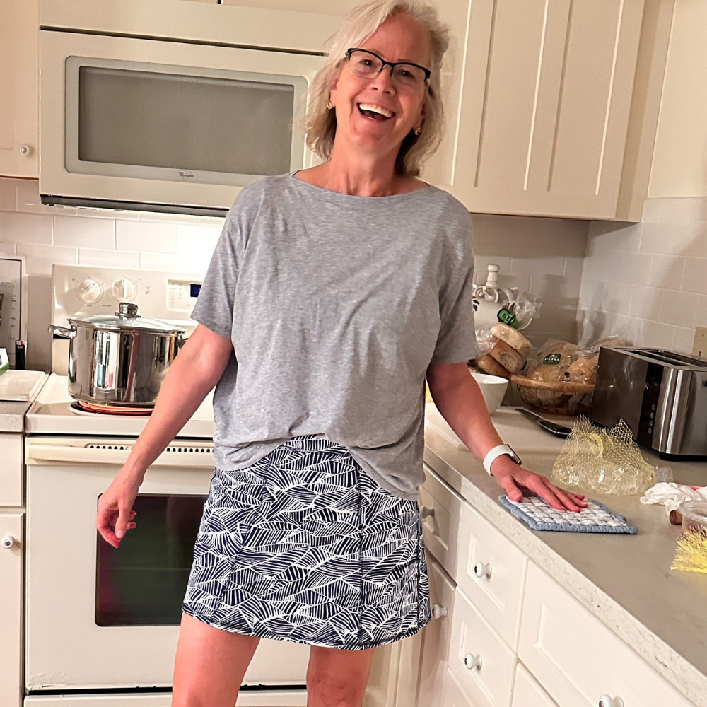 Woman standing in a kitchen wearing a grey shirt and Coastal Navy and white patterned skirt.