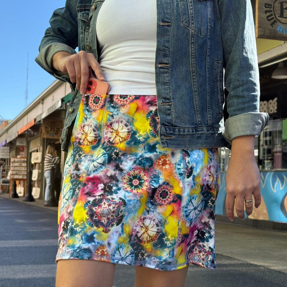 Person wearing a colorful tie-dye skirt with a denim jacket outdoors.