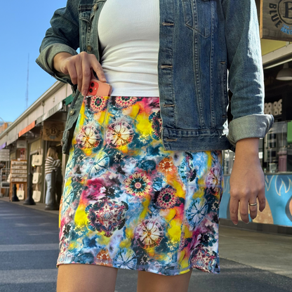 Person wearing a colorful tie-dye skirt with a denim jacket outdoors.