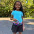 Young girl in a blue shirt and black skirt with a colorful BANDI Star Power belt standing outdoors.